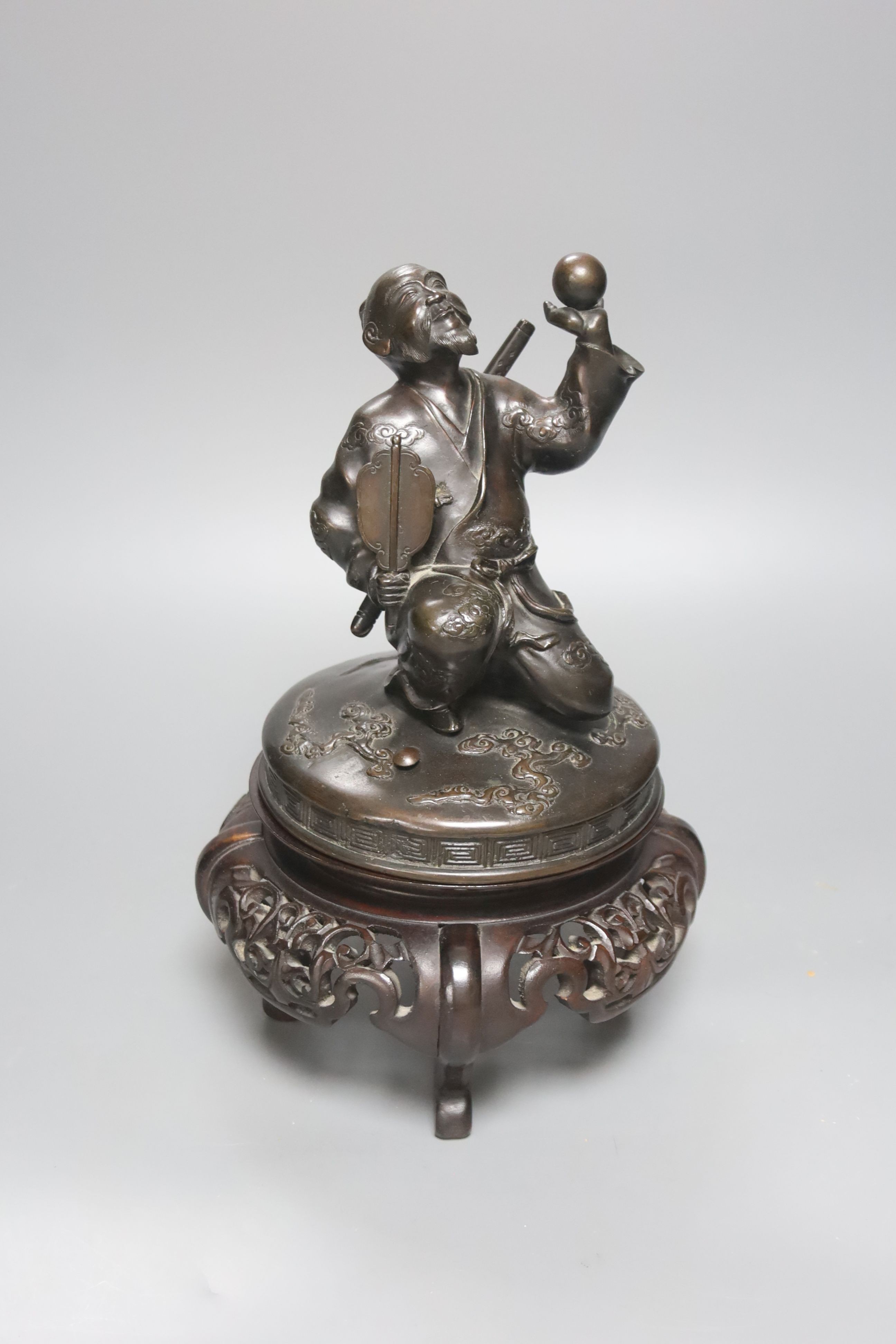 A Japanese bronze cover modelled as a samurai general, Meiji period, holding a fan and a ball, wood stand 28cm total height